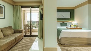 Quarto de hotel com cama, sofá, varanda e vista, e um quadro na parede.