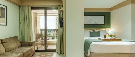 A hotel room with a bed, a sofa, a balcony with a view, and a painting on the wall.