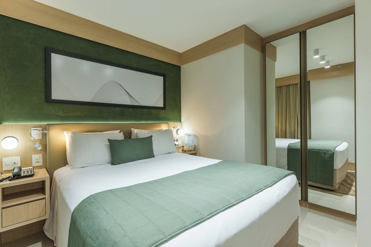 Habitación de hotel con una cama grande, una mesita de noche con un teléfono, una lámpara de noche y una obra de arte colgada en la pared.