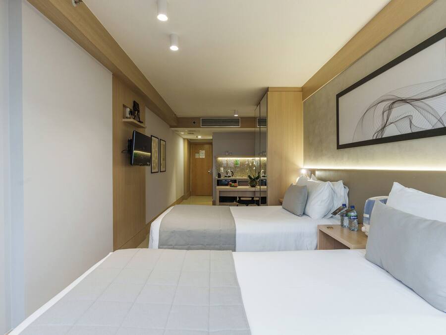 Habitación de hotel con dos camas, televisión, kitchenette y baño.