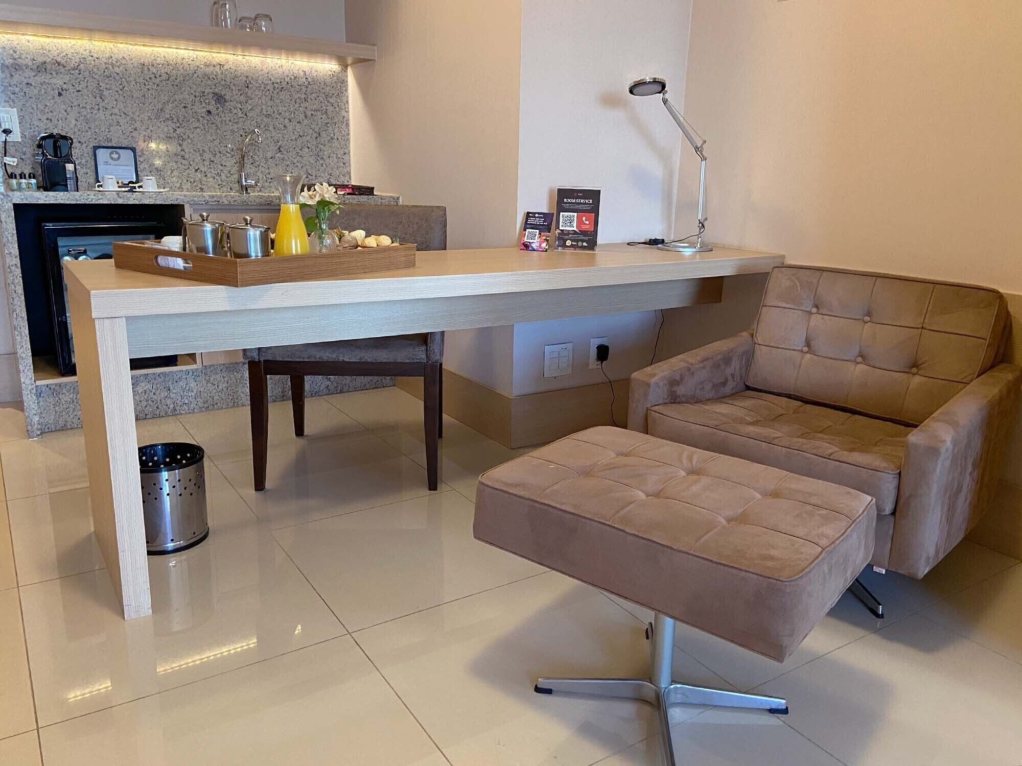 A modern living room with a long table, a cushioned armchair, a small side table, and a trash can.