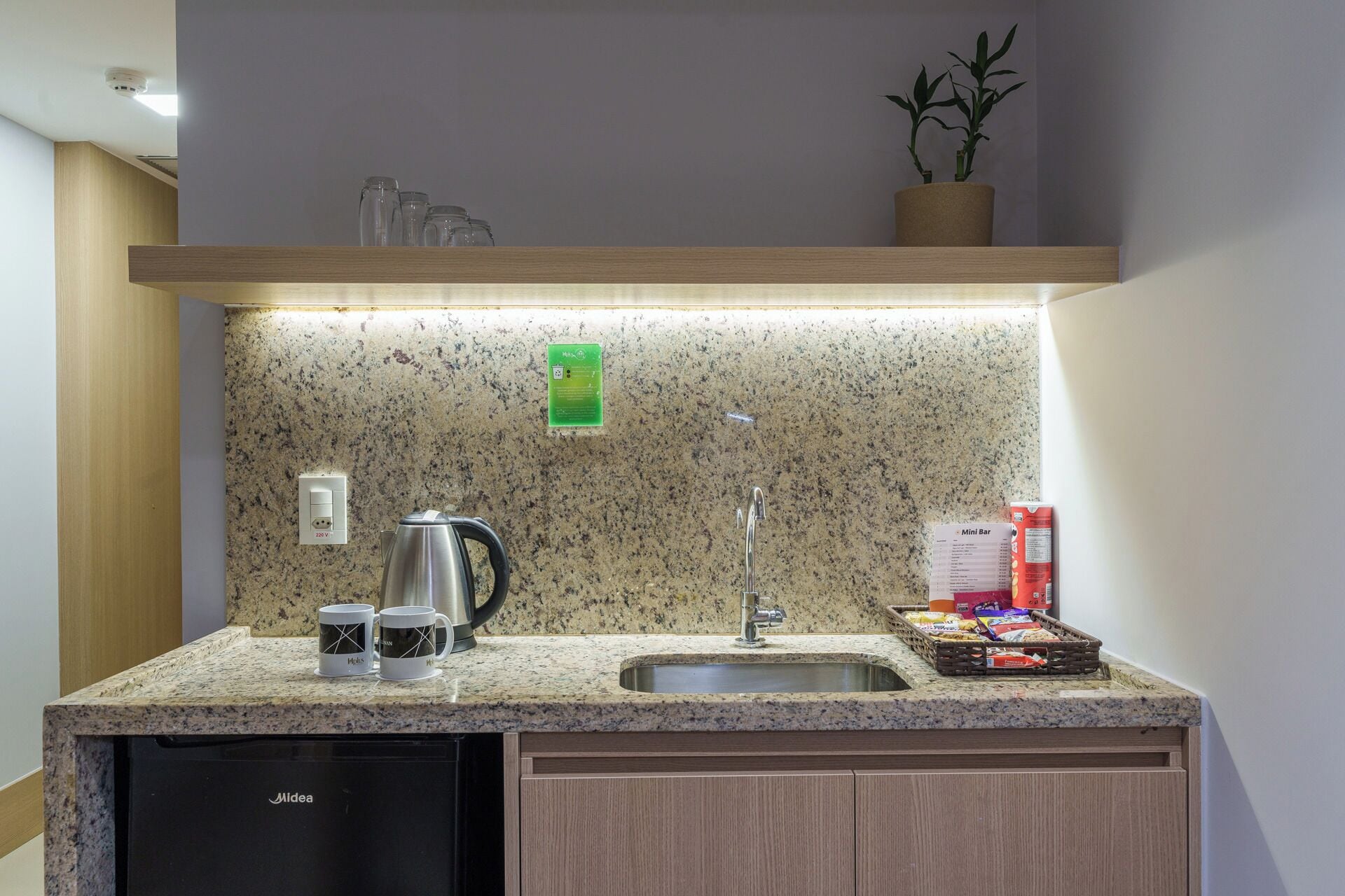 Une petite cuisine équipée d’un plan de travail en granit, d’une machine à café, d’une bouilloire, d’un évier et d’un mini-bar avec des collations.
