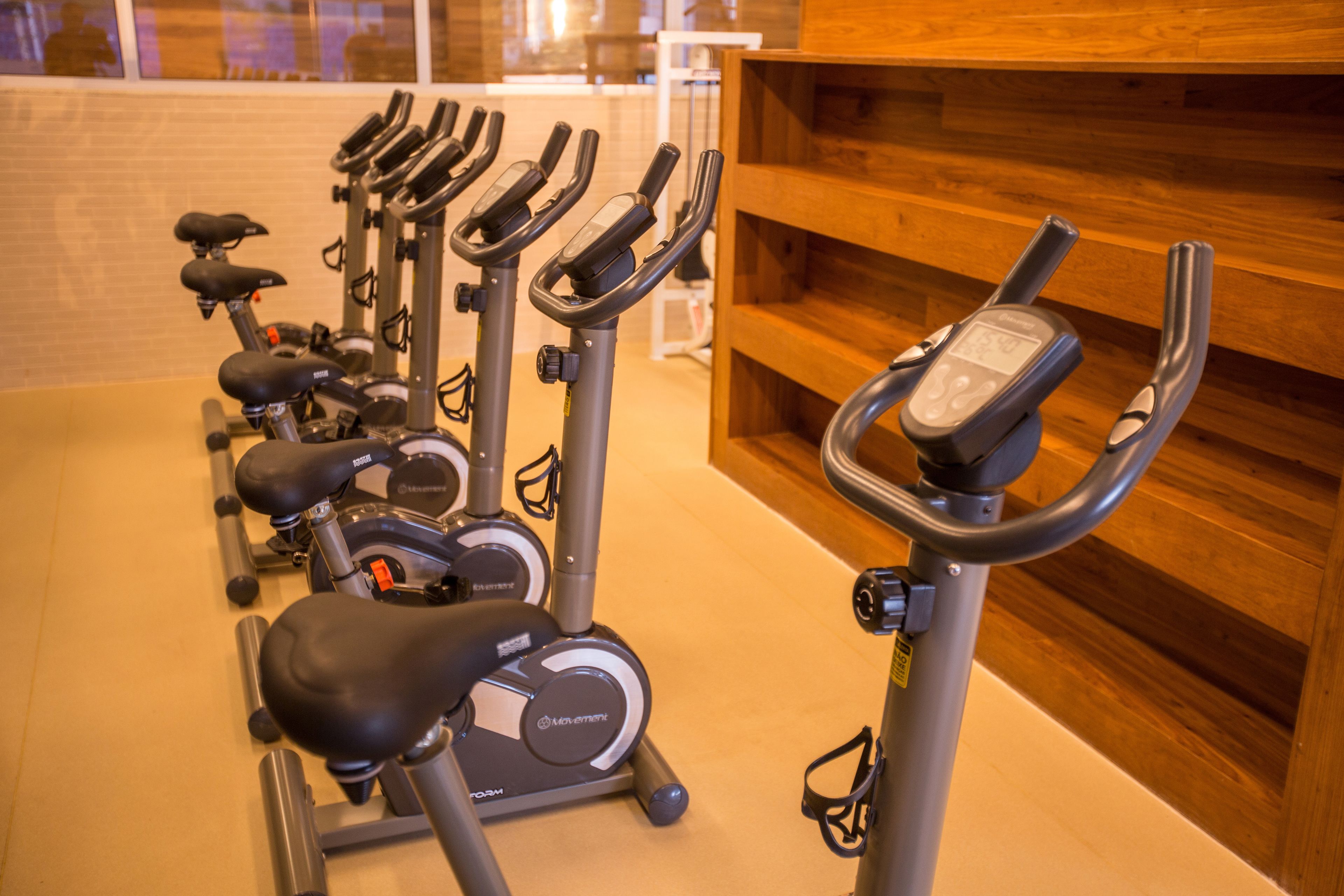 En række motionscykler i et fitnesscenter med træpaneler på væggene.