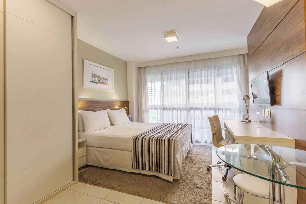Une chambre d’hôtel avec un lit, un bureau et une chaise, une télévision et une fenêtre avec des rideaux.