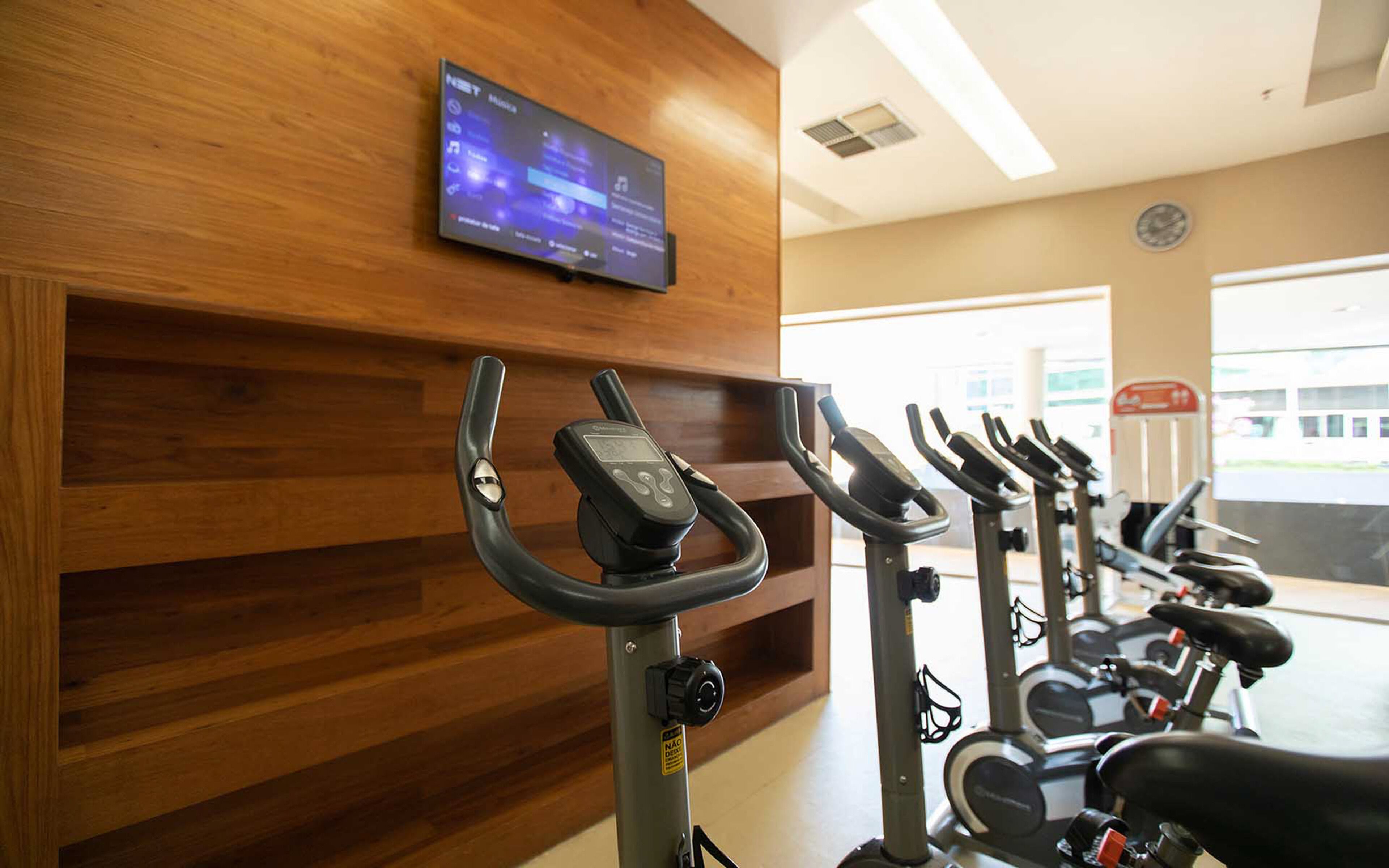 Une salle de sport équipée de plusieurs vélos d’appartement, d’un écran mural diffusant de la musique et d’un mur recouvert de panneaux en bois.