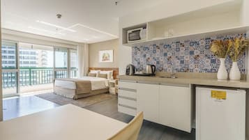Habitación de hotel moderna con cama, kitchenette, zona de comedor y vistas a la ciudad.