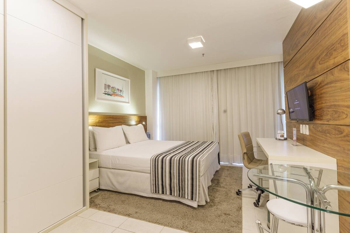 Une chambre d’hôtel comprenant un lit, un bureau avec une chaise, une télévision et un mur décoratif en bois.