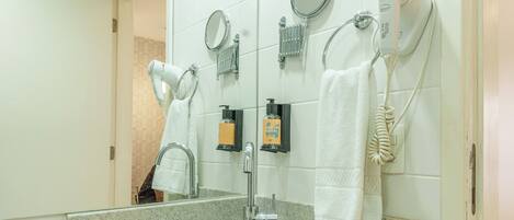 Un baño con un lavabo redondo, un espejo, un secador de pelo y un toallero.