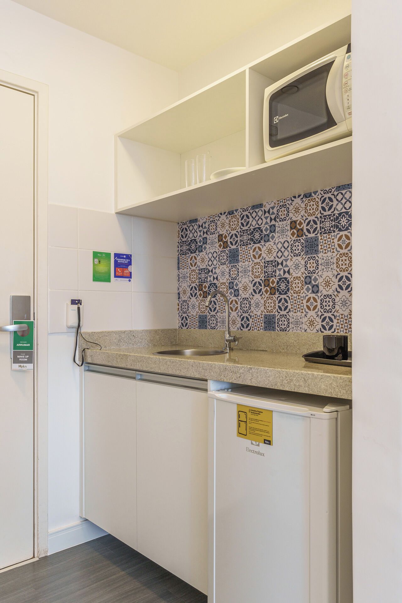 A compact kitchenette with a microwave, sink, and patterned backsplash.