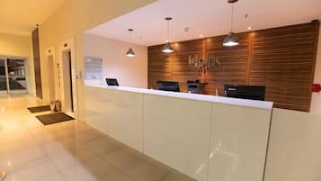 A reception area with a white reception desk, three black computers, and wooden paneling on the wall.