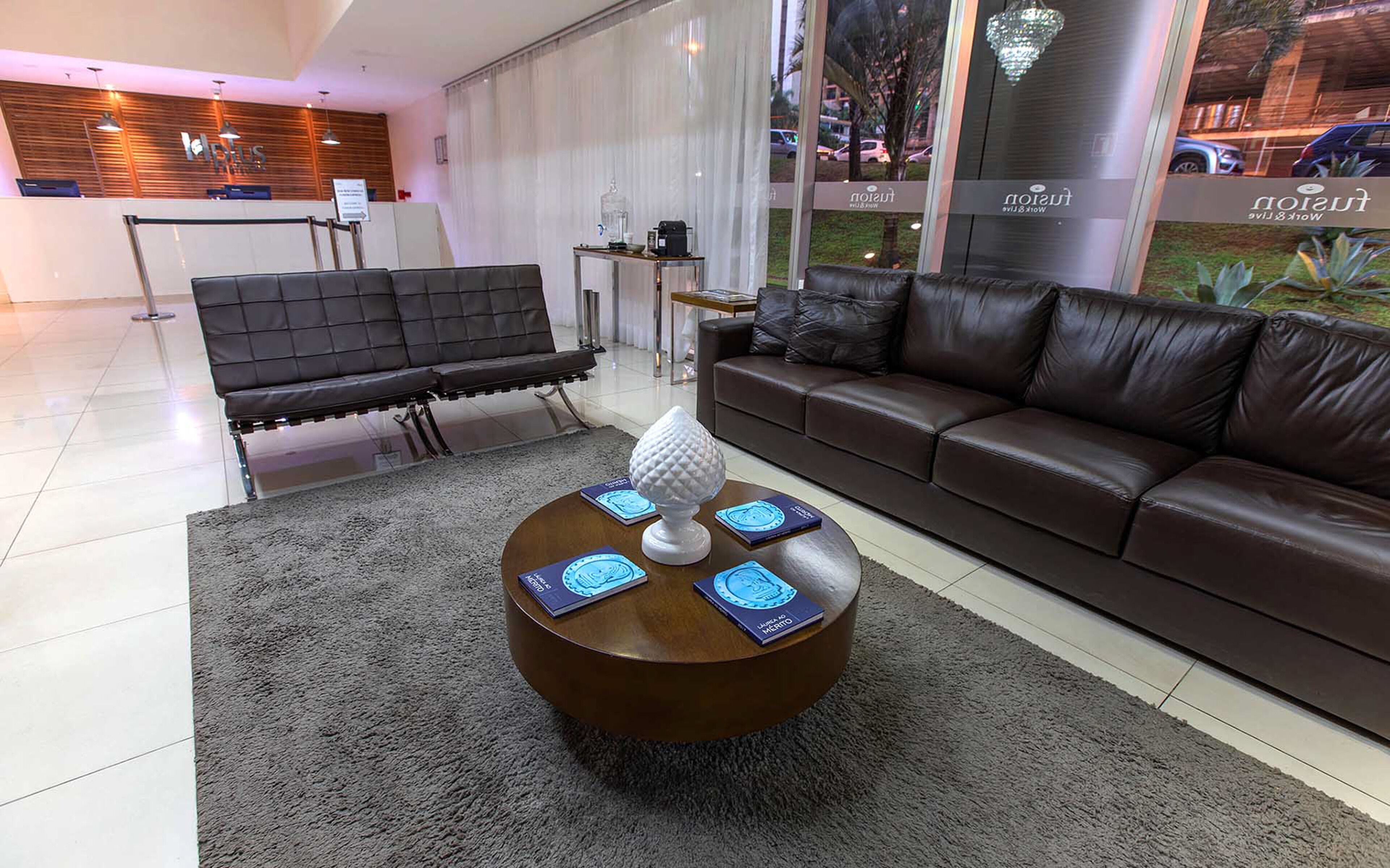 Un moderno vestíbulo de hotel con un sofá de cuero, una mesa de centro redonda con objetos decorativos y un mostrador de recepción.