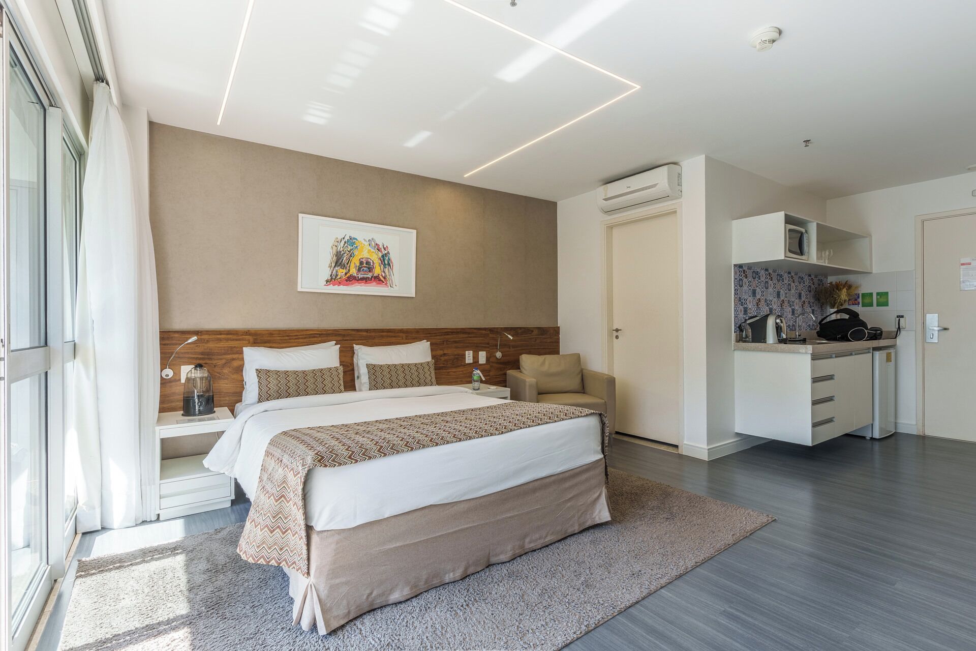 Une chambre d’hôtel moderne équipée d’un grand lit, d’un petit canapé, d’une kitchenette et d’une salle de bain.