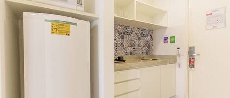 A kitchen with a microwave, a refrigerator, a sink, and patterned backsplash tiles.