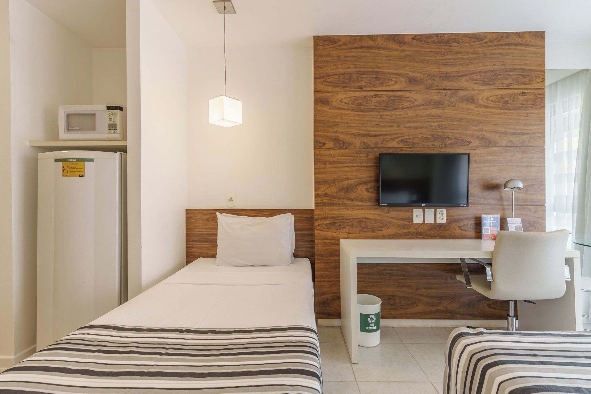 A hotel room with a bed, a desk, a chair, a TV, a microwave, and a refrigerator.