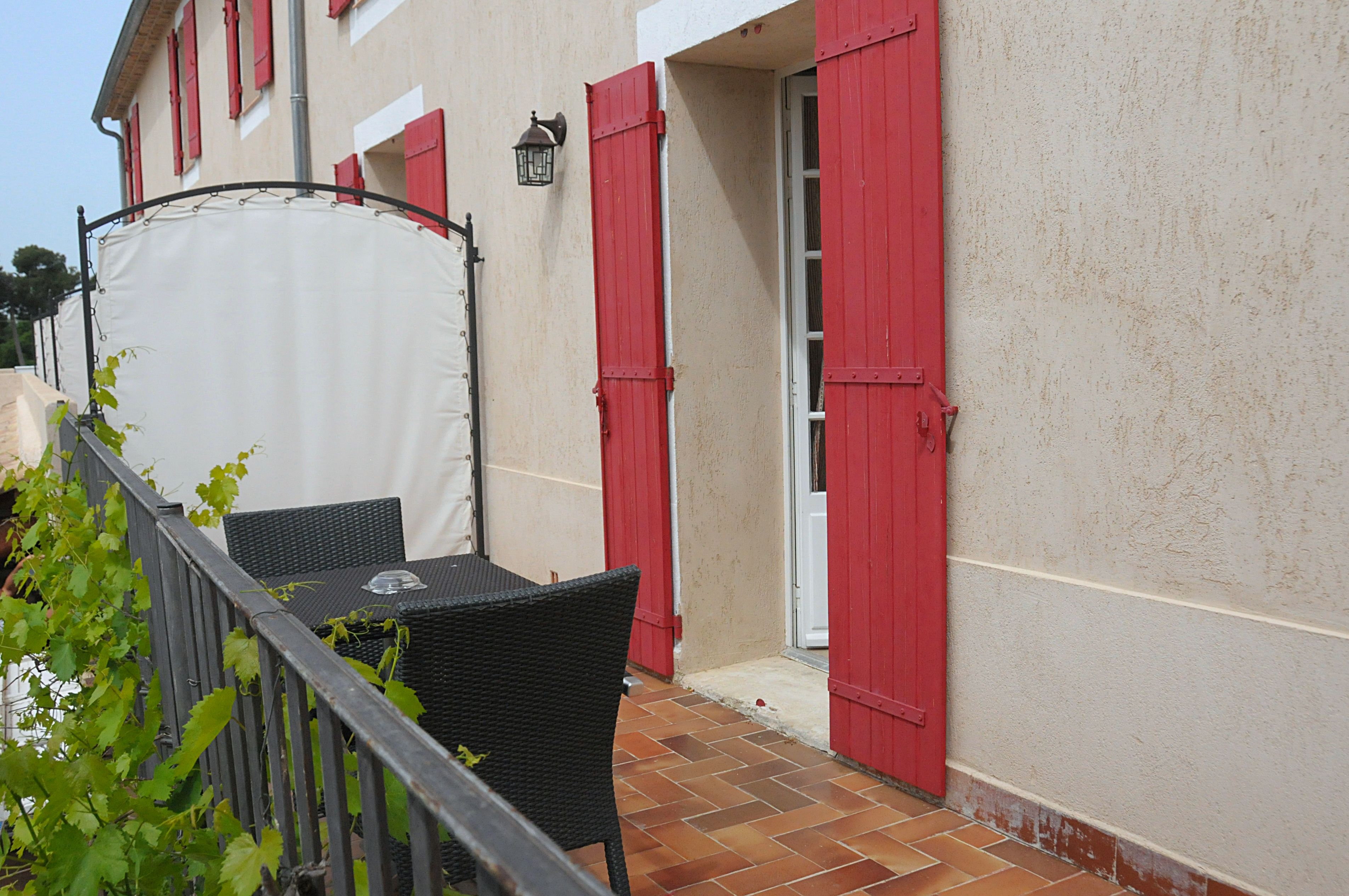 Un patio con una mesa y sillas, una carpa blanca y contraventanas rojas en un edificio.