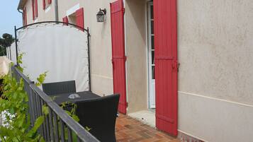 Un patio con una mesa y sillas, una carpa blanca y contraventanas rojas en un edificio.