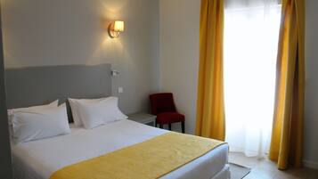 Habitación de hotel con cama, almohadas blancas, un plaid amarillo, una silla roja y una ventana con cortinas amarillas.