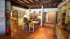 Una cocina con una mesa de madera, sillas y una maleta roja. Hay un mapa en la pared y una estantería con botellas.