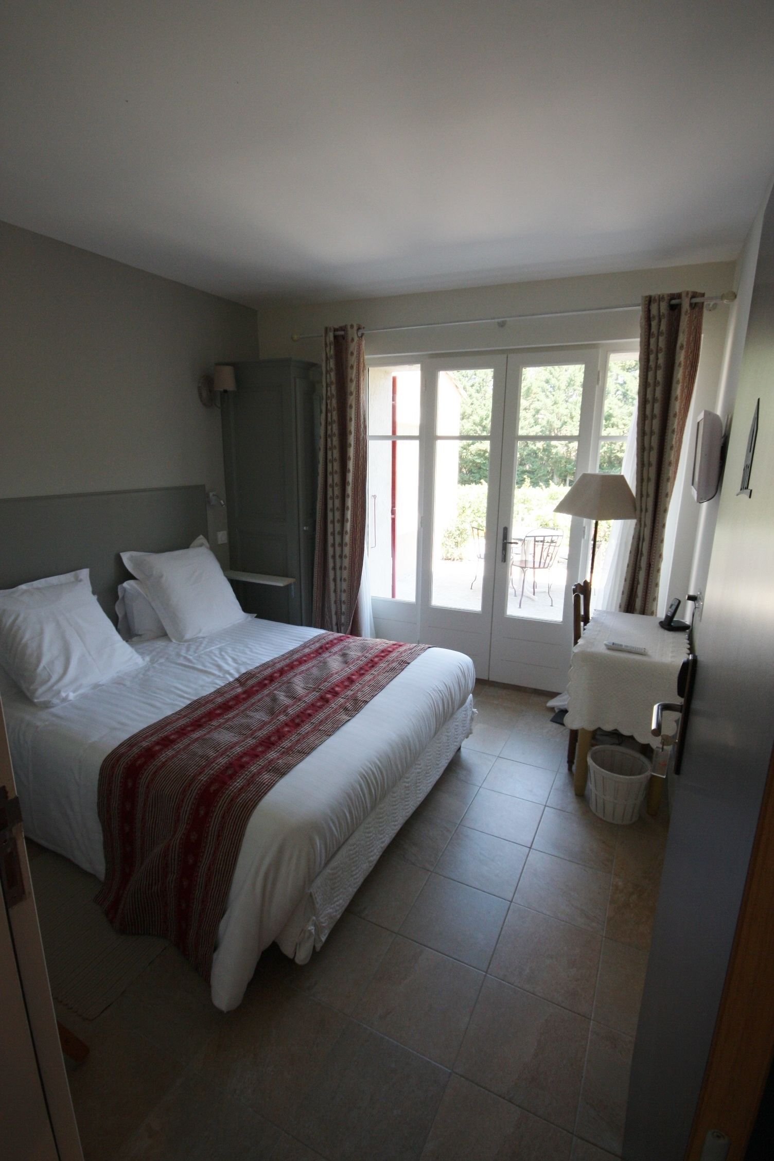 A hotel room with a bed, a desk, a chair, a lamp, and a view of the outdoors through a glass door.