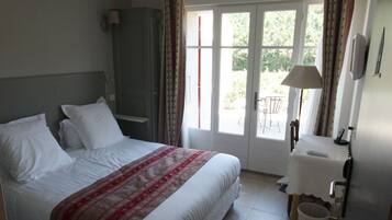 A hotel room with a bed, a desk, a chair, a lamp, and a view of the outdoors through a glass door.