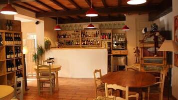 Un interior rústico con mobiliario de madera, una zona de bar con estantes llenos de botellas e iluminación colgante.