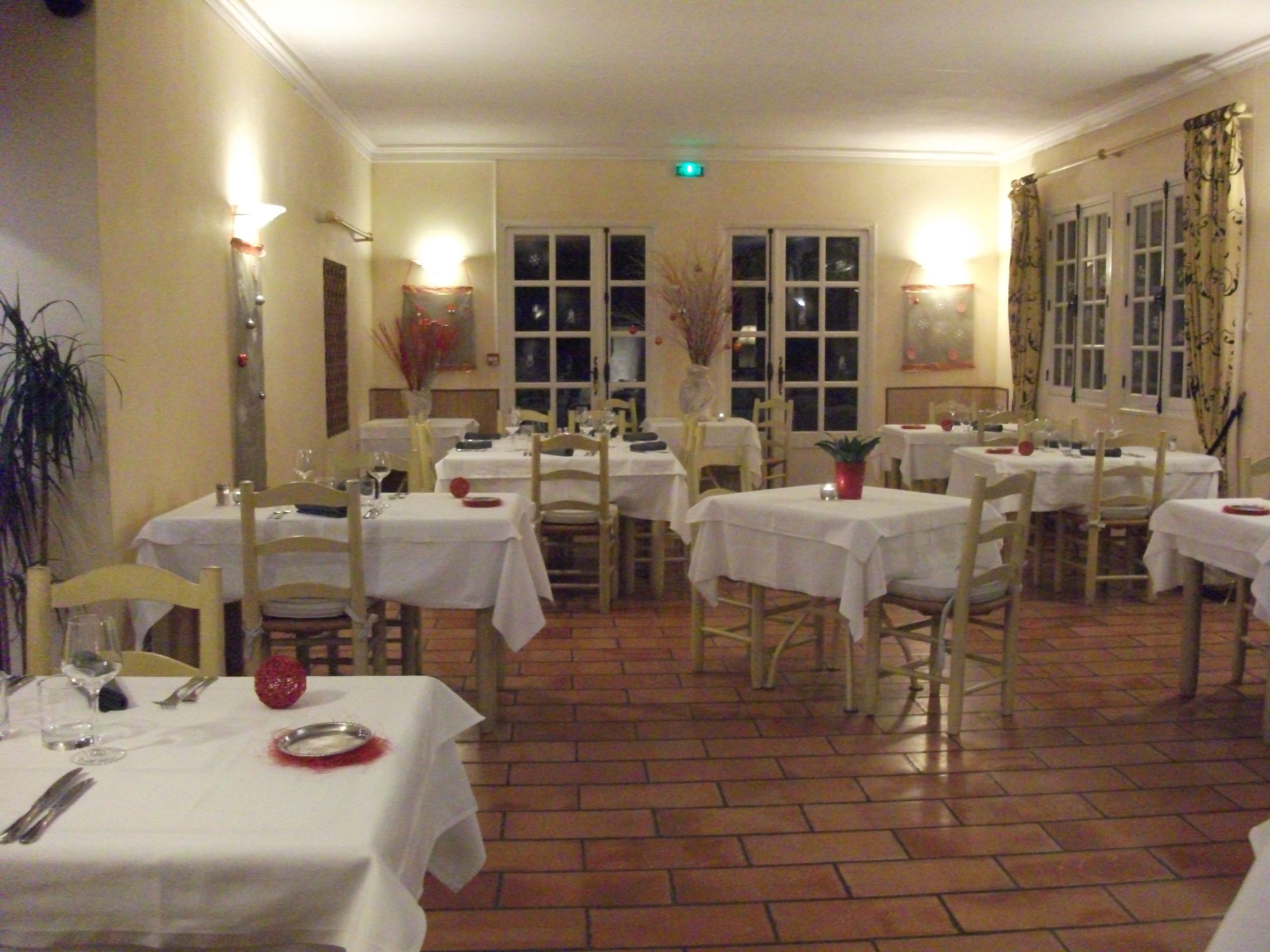 A dining area with multiple tables set for service, featuring white tablecloths and chairs, and a tiled floor.