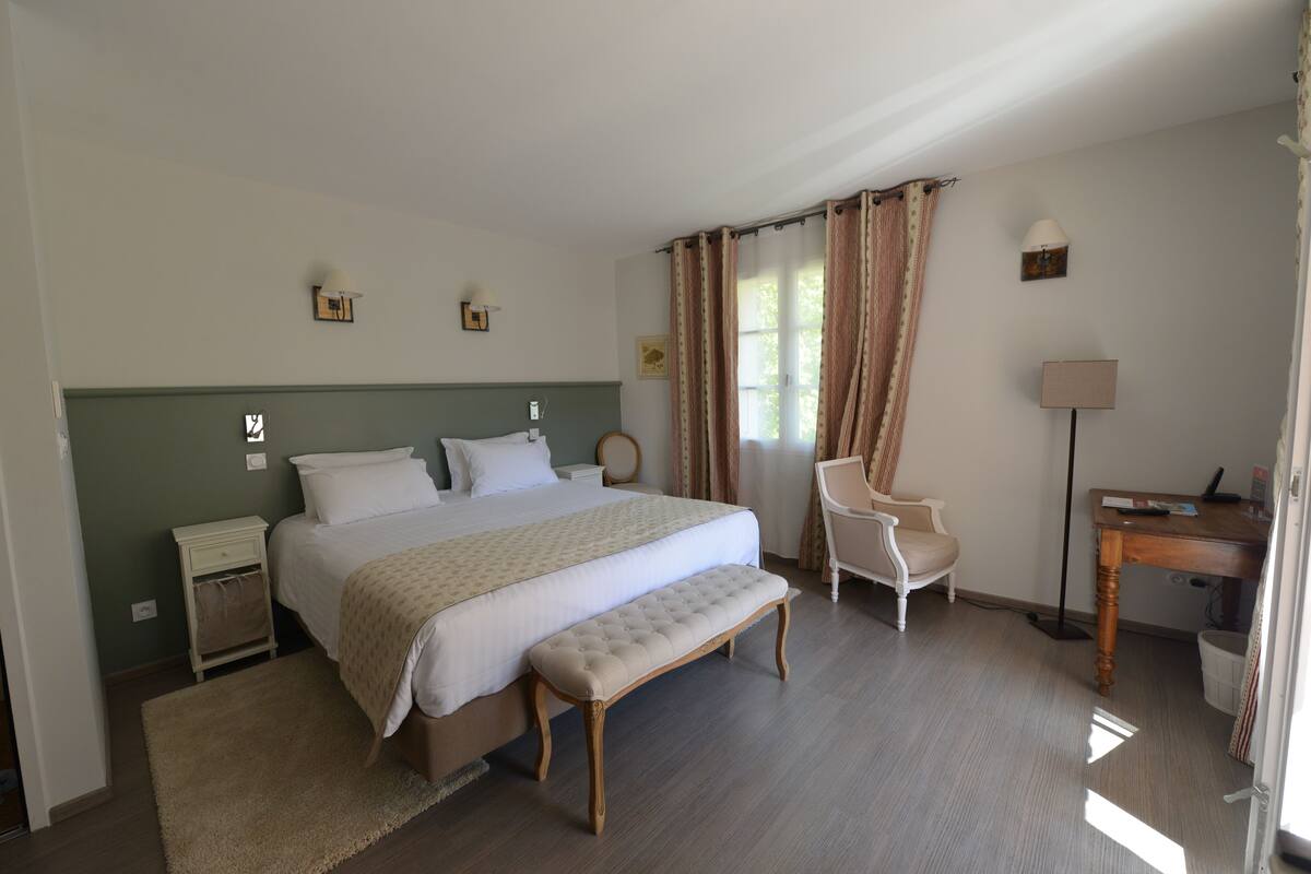 A neatly arranged bedroom with a large bed, a bedside table, a chair, and a desk.