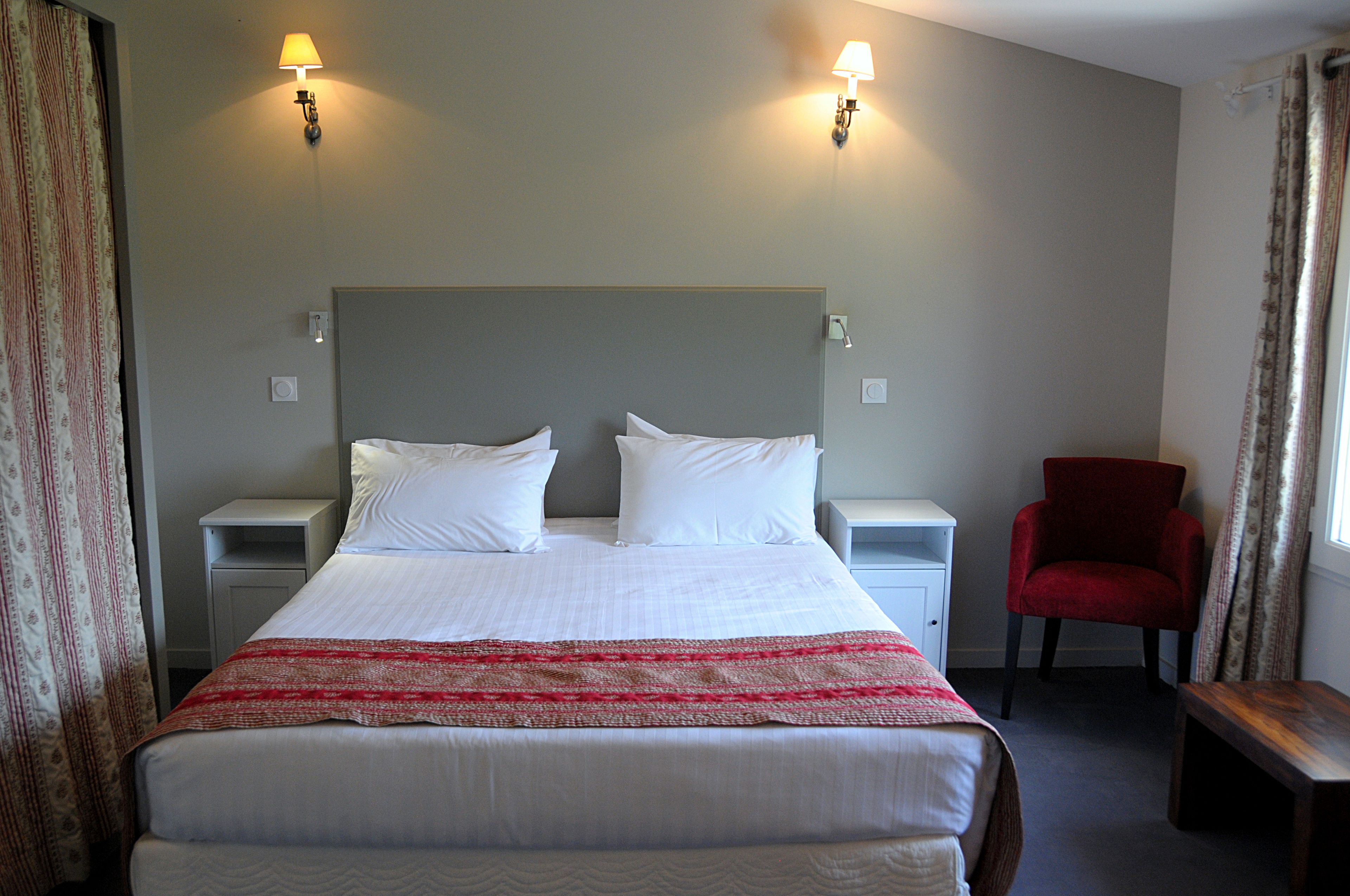 A hotel room with a large bed, two bedside tables, a red chair, and two wall-mounted lamps.