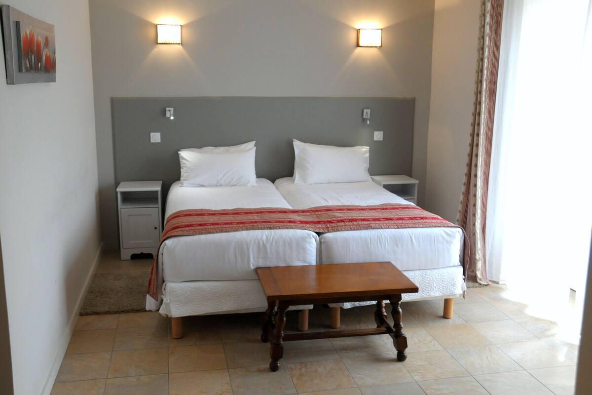 A double bed with a wooden nightstand, a small table, and two wall-mounted lights.