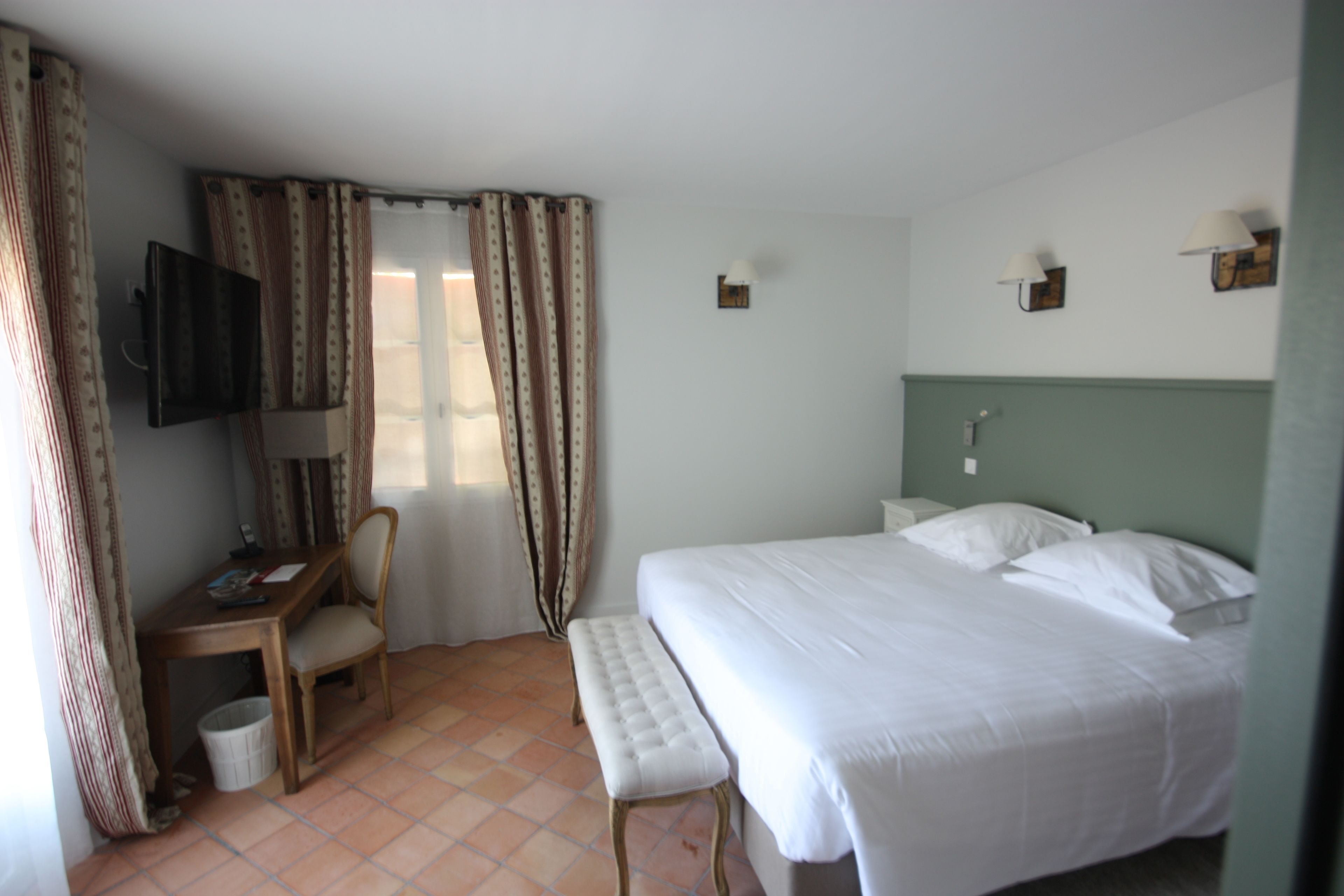 A hotel room with a bed, a desk, a chair, a television, and a window with curtains.