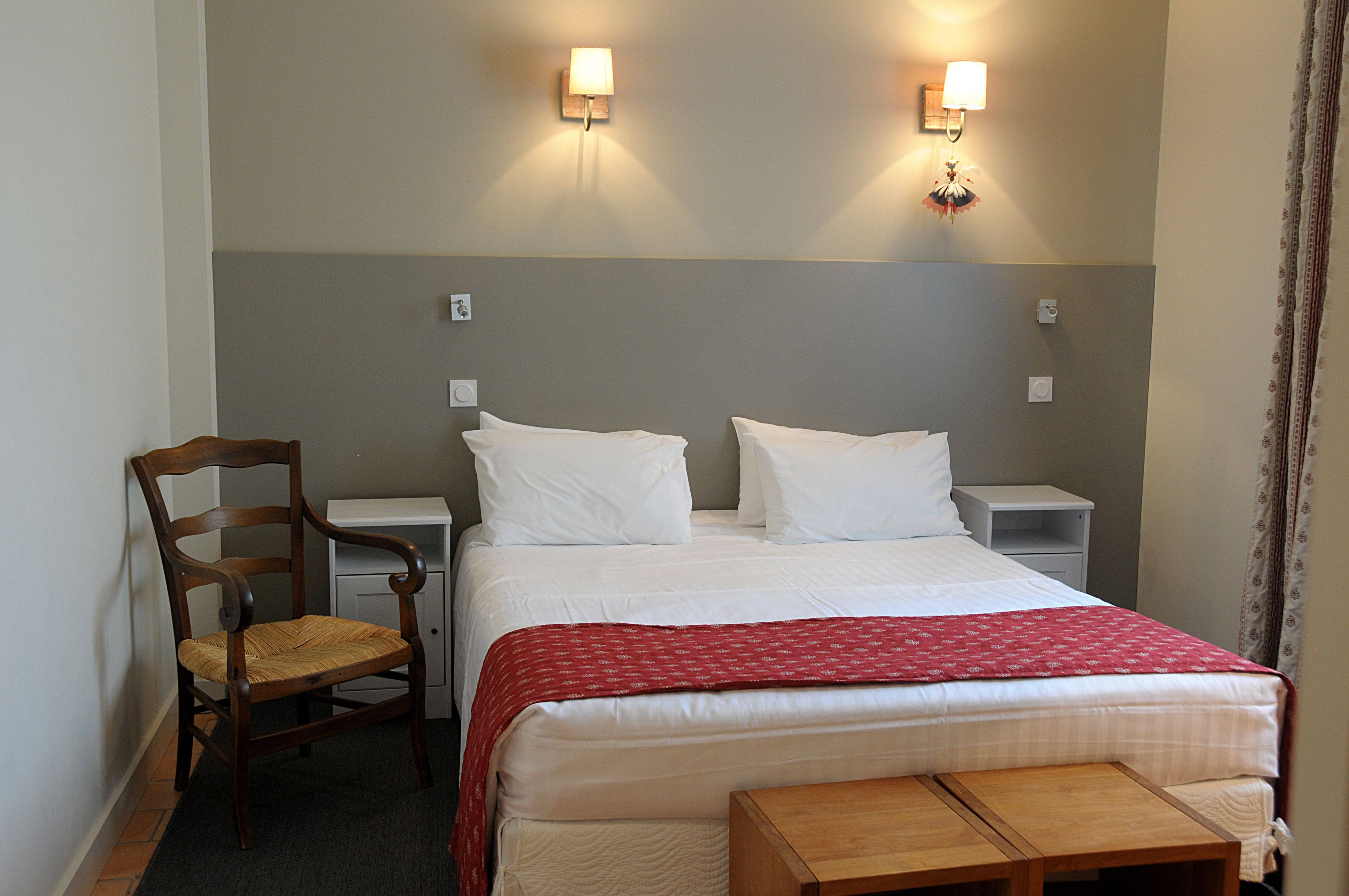 Ett hotellrum med en säng, två sängbord, en stol och ett litet träbord.