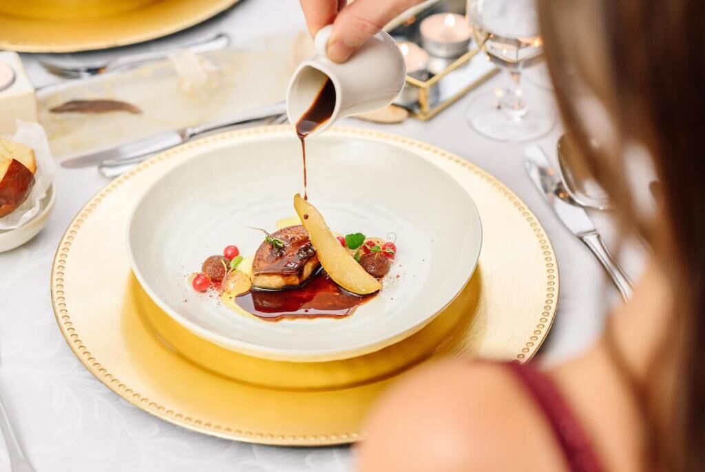 A person pouring sauce onto a dish with vegetables and fruit.