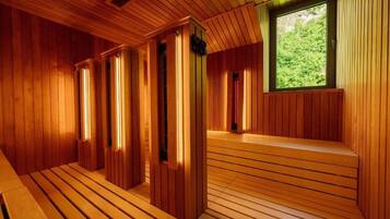 A sauna with wooden walls and benches, a window with a view of greenery, and a small ventilation opening.
