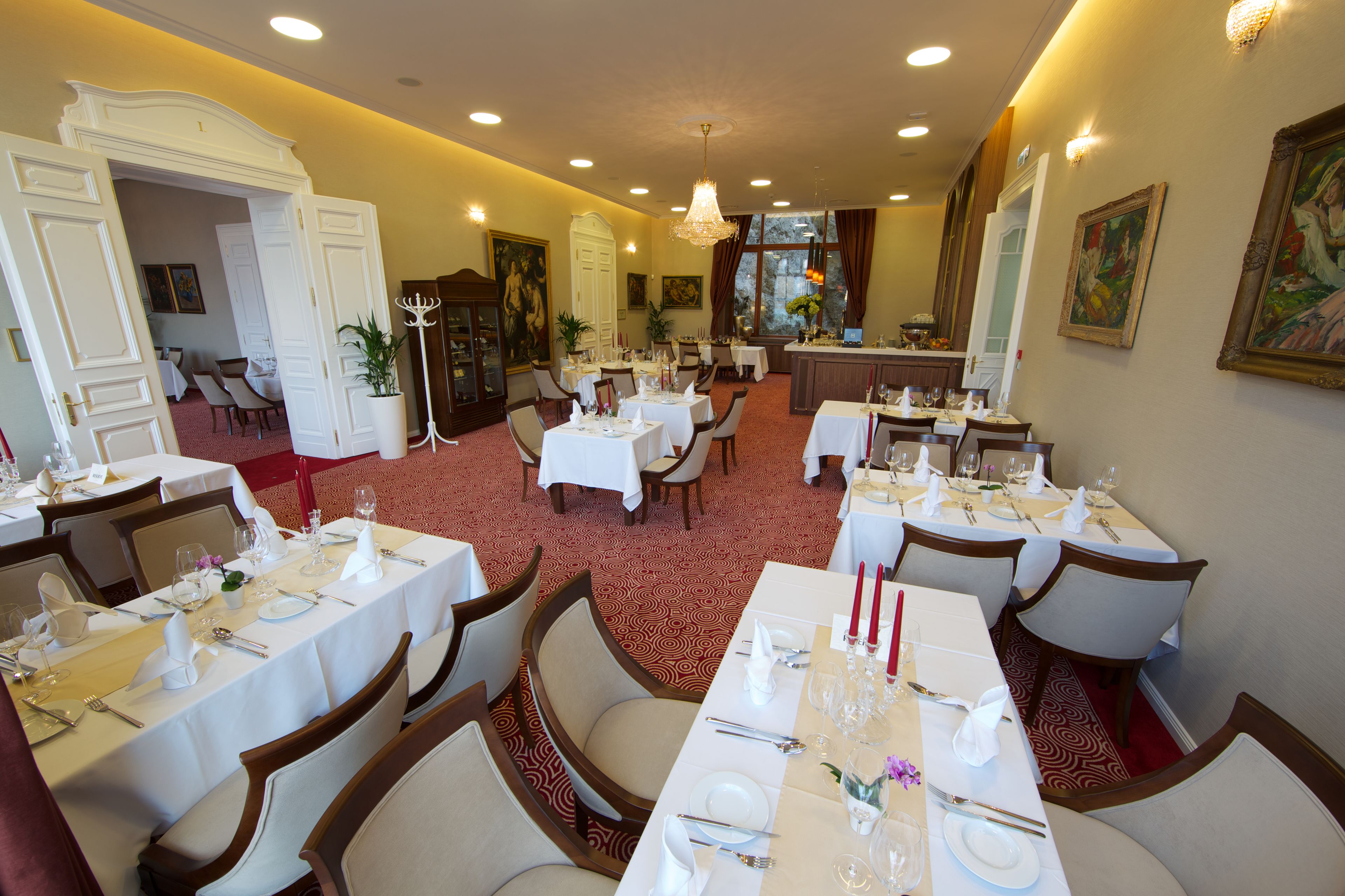 A formal dining room with multiple tables set for service, a chandelier, and classic decor.