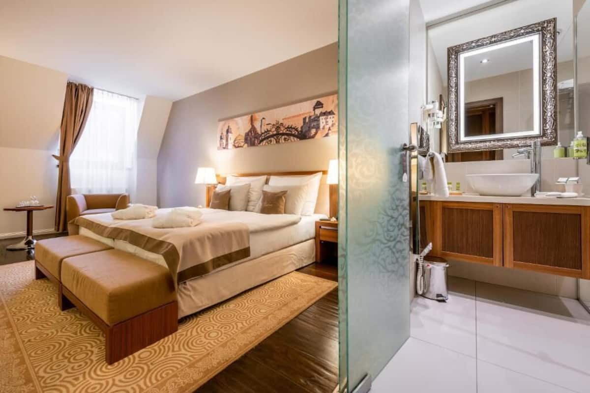 Una habitación de hotel con cama, mesita de noche, lámpara y un espejo grande.