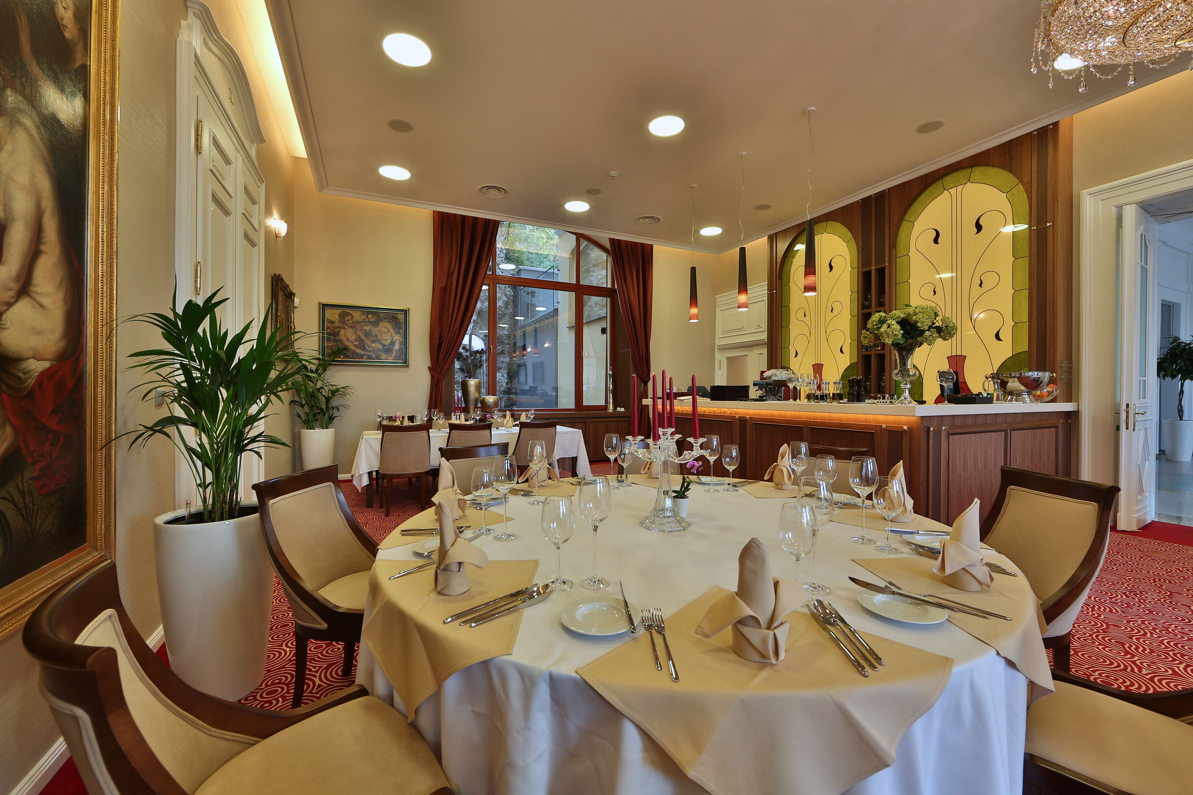 A dining area with a long table set for a meal, surrounded by chairs, with a potted plant and artwork on the walls.