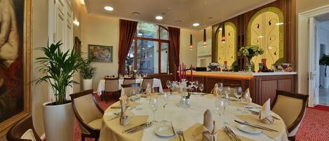Comedor con una larga mesa dispuesta para una comida, rodeada de sillas, una planta en maceta y obras de arte en las paredes.