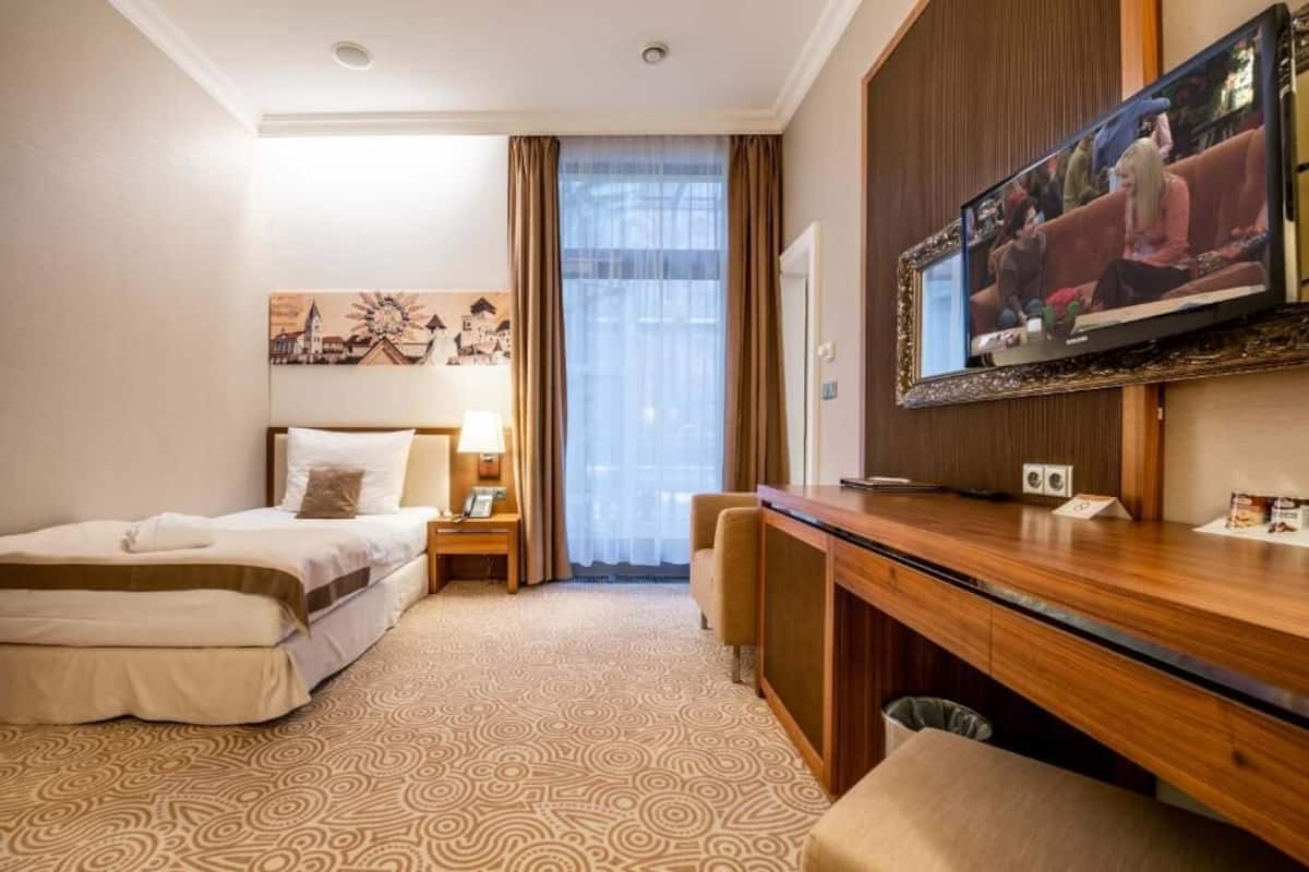 Una habitación de hotel con una cama, un escritorio, un televisor y un ventanal con cortinas.