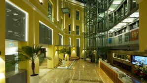 A modern hotel lobby with a marble floor, a reception desk, a seating area, and a glass elevator. - Hotel Elizabeth (Trencin)