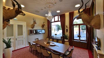 Uma sala de jantar com lustre, chifres de animais pendurados, uma mesa grande e cadeiras.