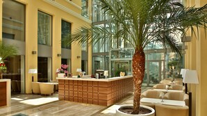 A modern lobby with a reception desk, seating area, and a large potted palm tree. - Hotel Elizabeth (Trencin)