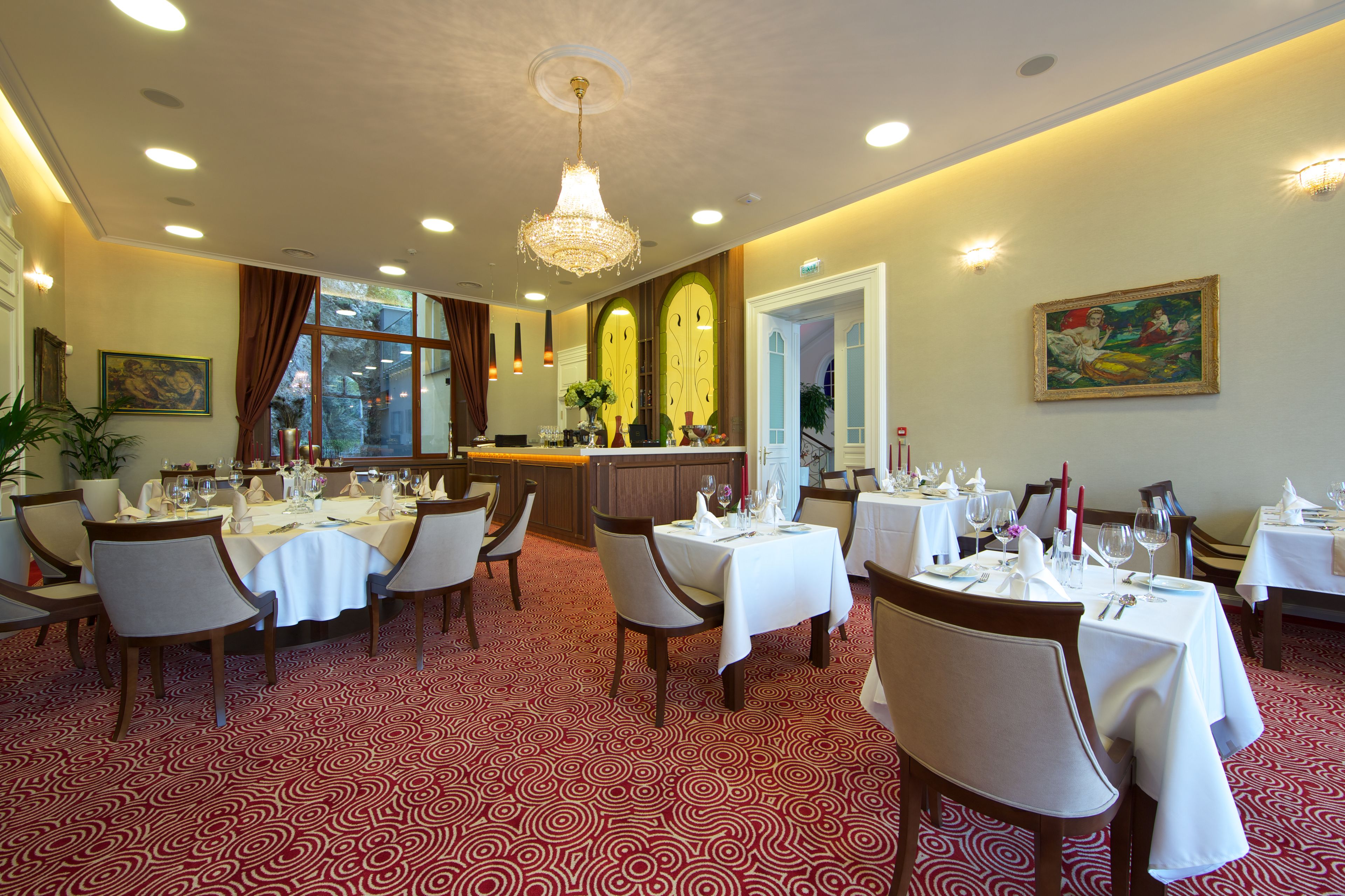 A restaurant with tables set for dining, a chandelier, and a painting on the wall.