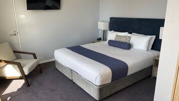 A hotel room with a bed, a chair, a TV, and a nightstand.