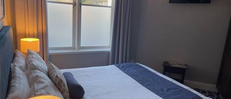 A hotel room with a bed, a TV mounted on the wall, and a window with curtains.