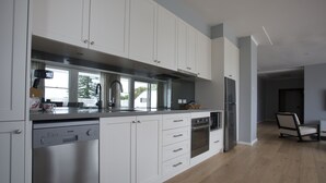A modern kitchen with white cabinetry, stainless steel appliances, and a large window. - Seabreeze Hotel (Nelson Bay)
