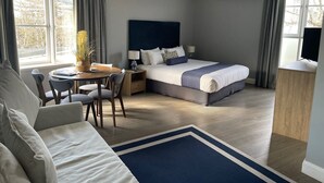 A modern hotel room with a large bed, a desk with a chair, a dining table, and a TV. - Seabreeze Hotel (Nelson Bay)