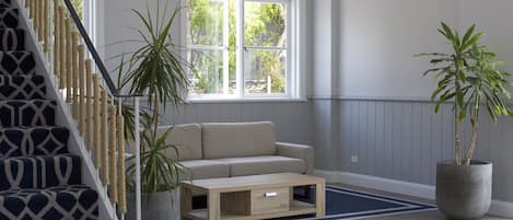 Uma escada com padrão geométrico, um sofá bege, uma mesa de centro de madeira e duas plantas em vasos.