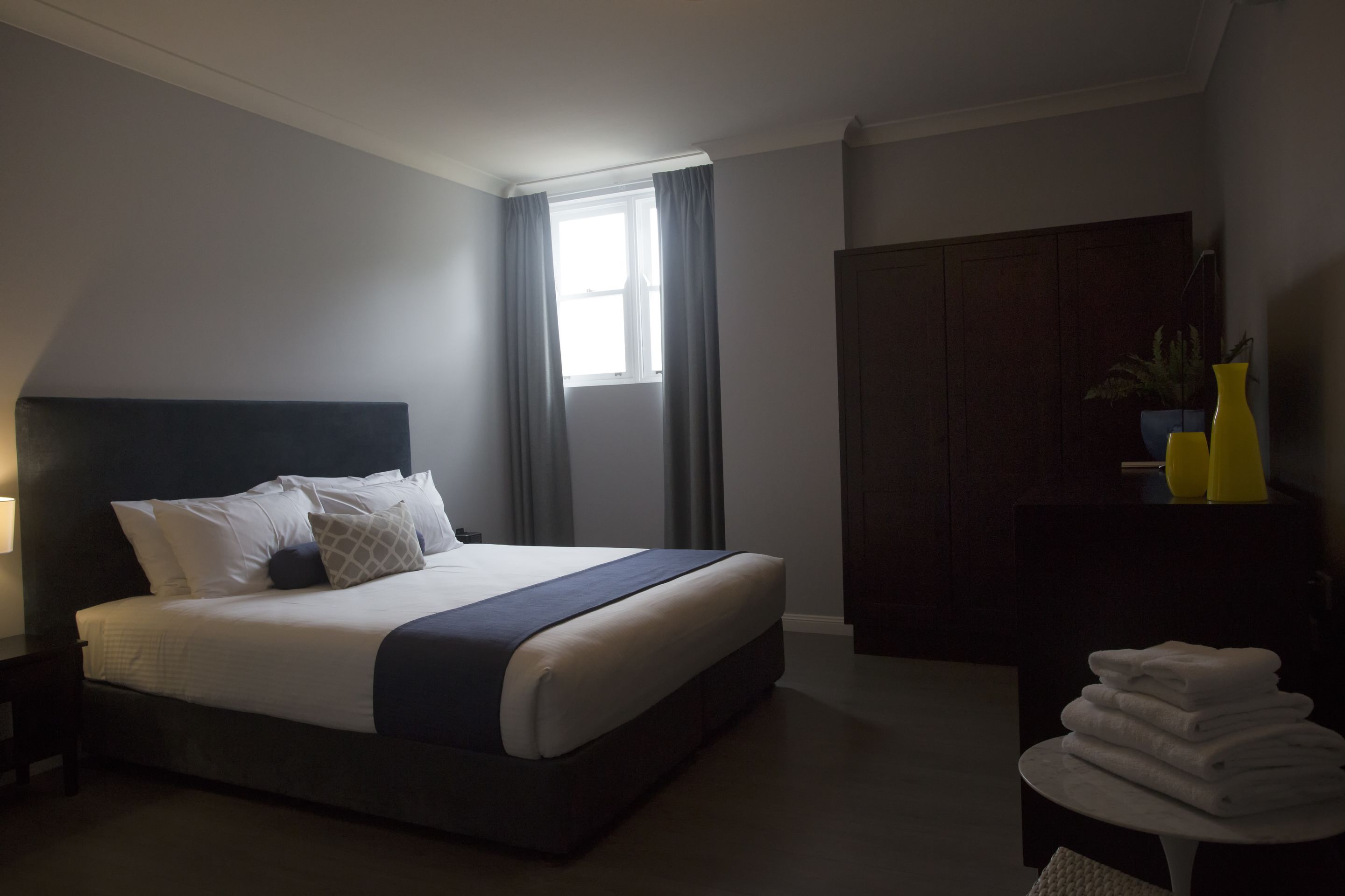 Ein modernes Hotelzimmer mit einem großen Bett, einem Nachttisch, einem Kleiderschrank und einem kleinen Tisch mit Handtüchern.
