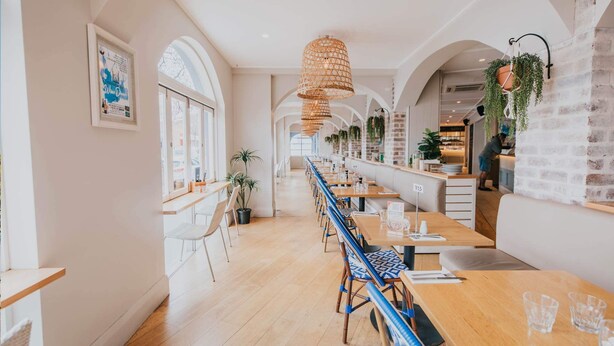 A long dining area with wooden tables and chairs, arched windows, and hanging plants. - Seabreeze Hotel (Nelson Bay)