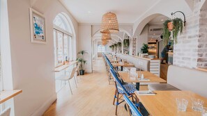 A long dining area with wooden tables and chairs, arched windows, and hanging plants. - Seabreeze Hotel (Nelson Bay)
